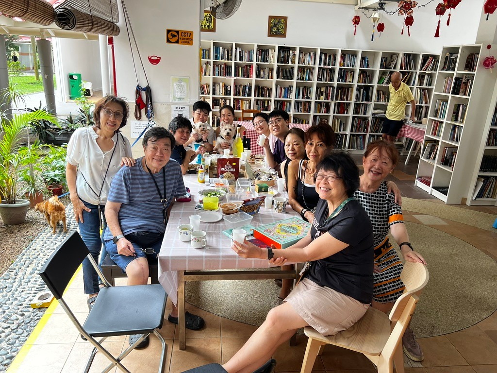 A group of neighbours and three small dogs gathered around a long table inside the library